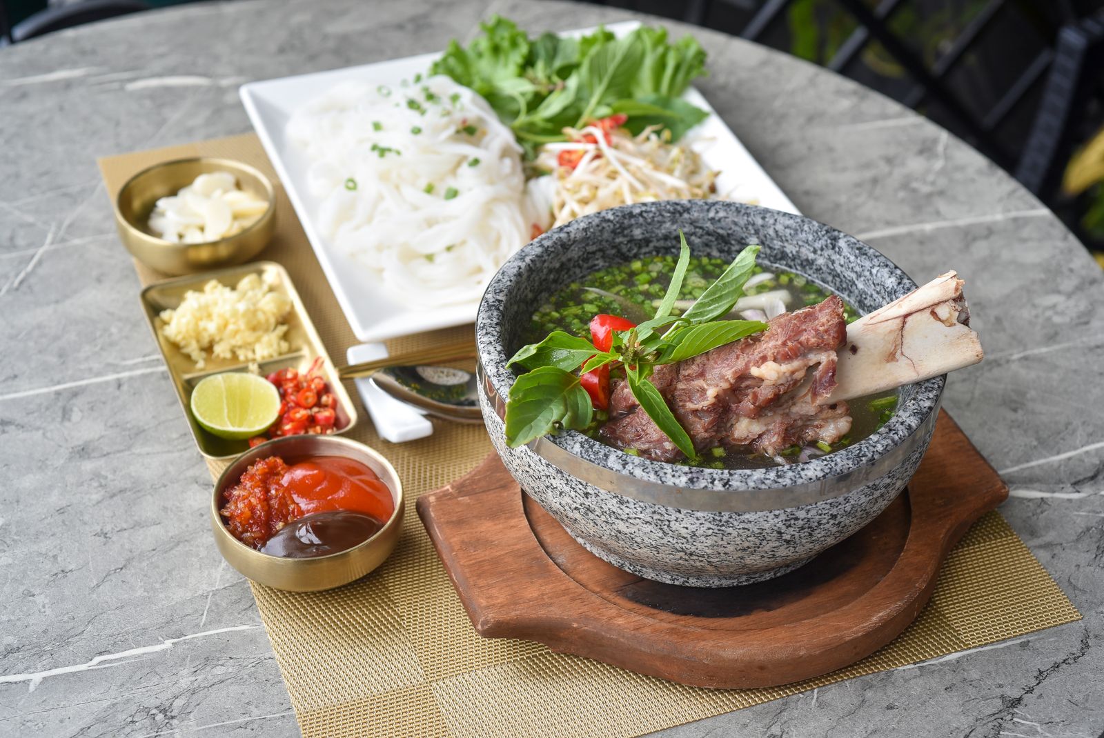 Beef rib pho in a stone bowl with herbs and sauces