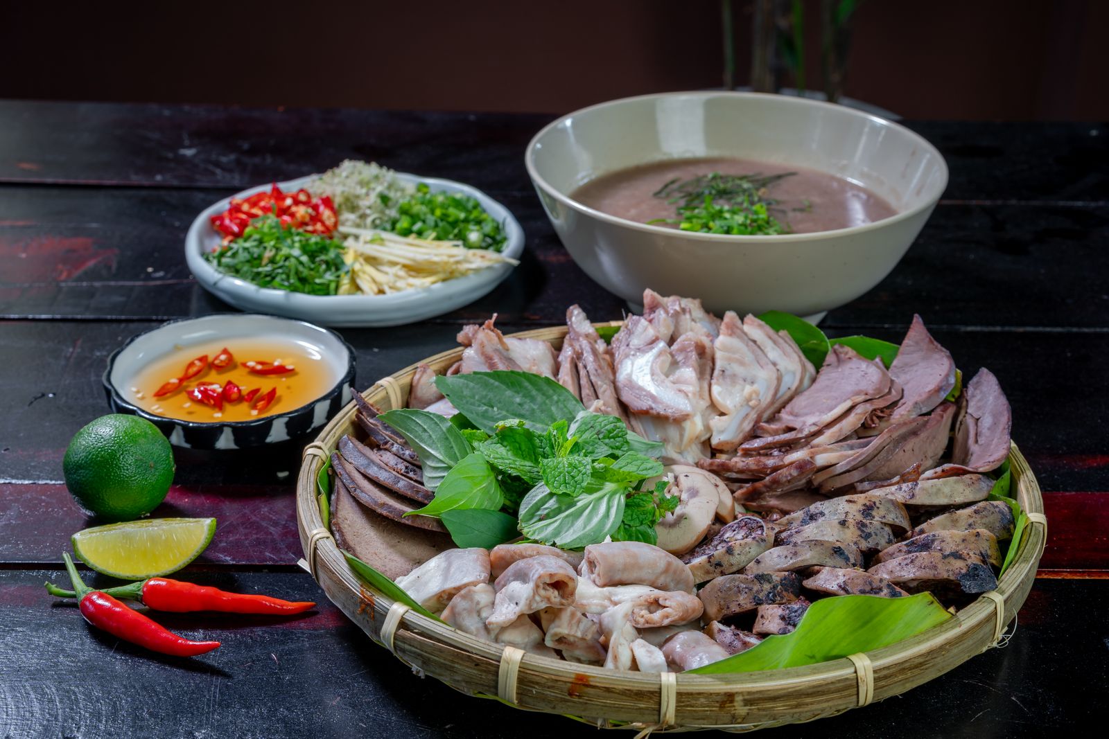Dark table set with pho, a platter of sliced beef and fresh herbs